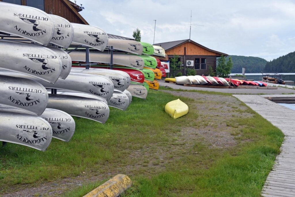 Canoes stacked on grass beside lake at Opeongo Outfitters in Algonquin Provincial Park.